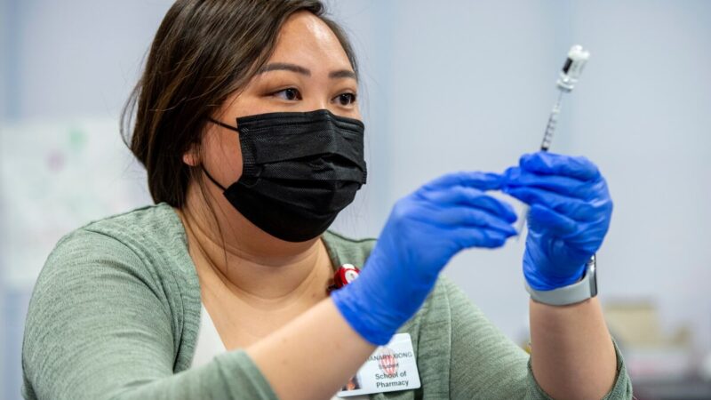 Phanary Xiong, wearing a mask and blue gloves, holds a vaccine needle