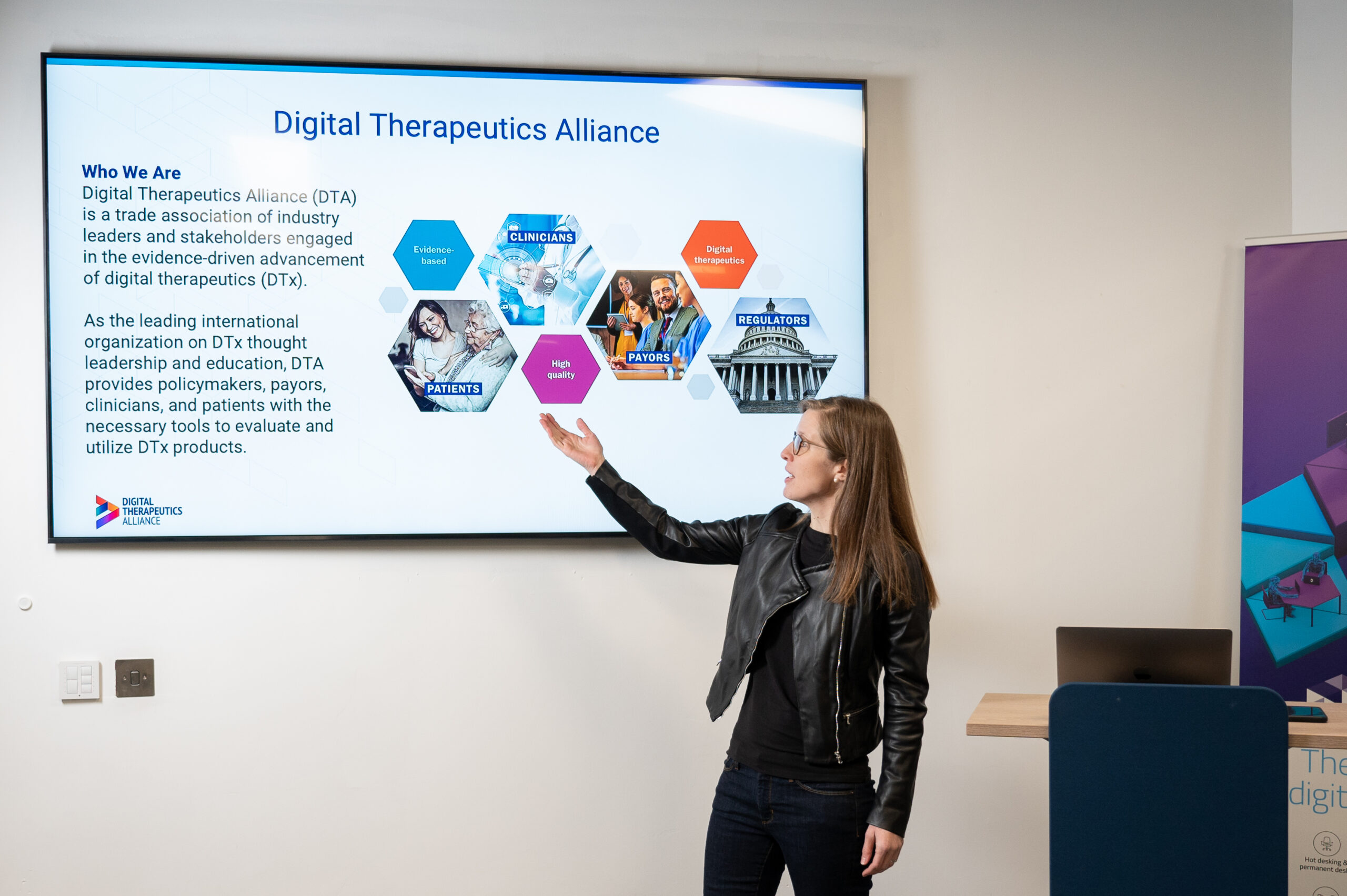 Megan Coder gestures to a screen with information about the Digital Therapeutics Alliance.
