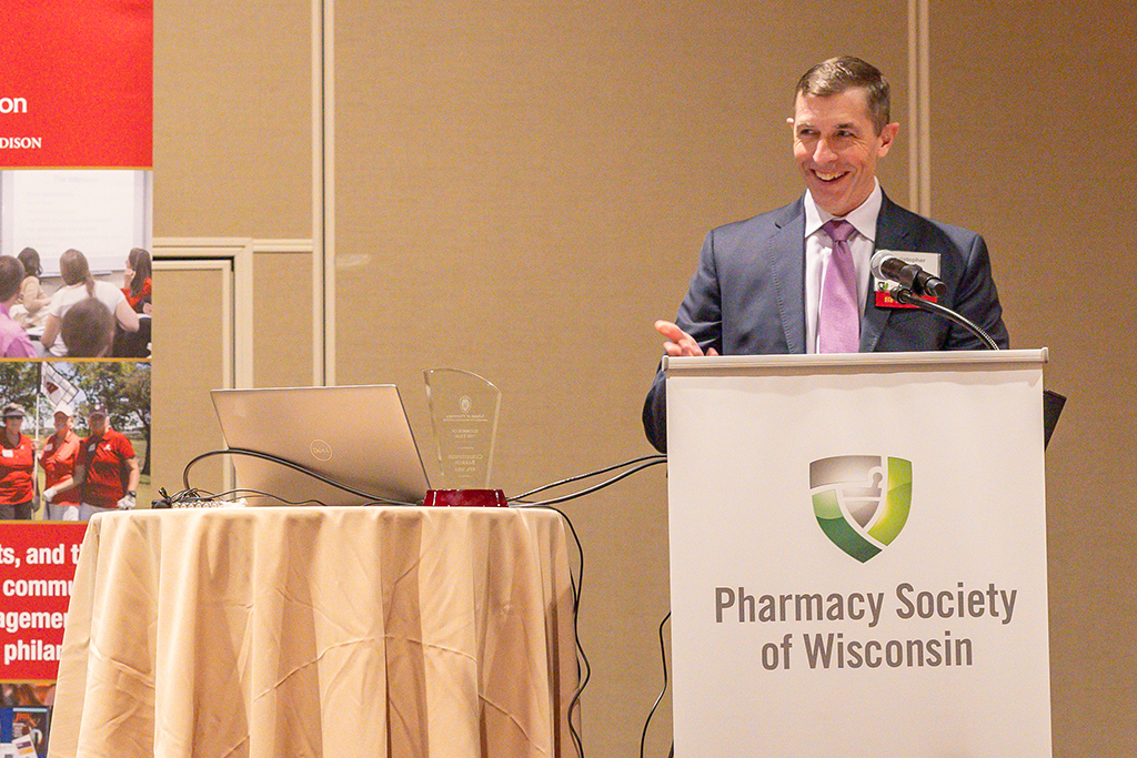 Chris Barron speaks at a podium marked with the Pharmacy Society of Wisconsin logo