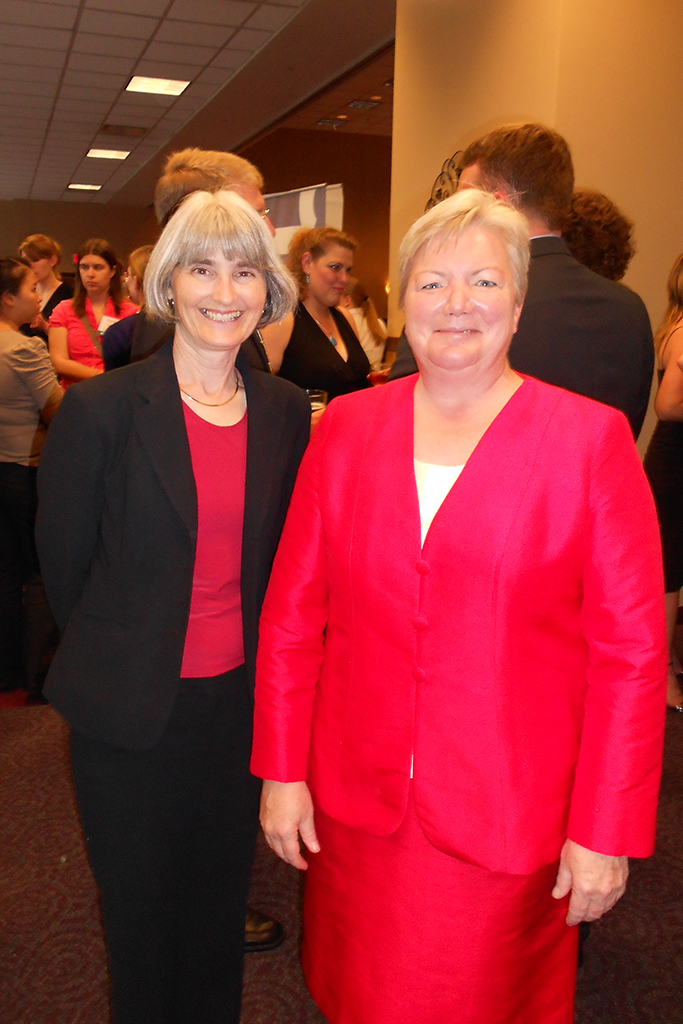 Mara Kieser and Jeanette Roberts, both in red, in a room with people behind them