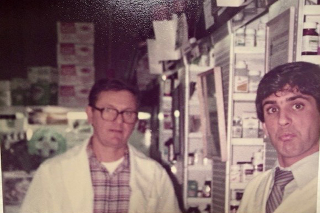 An old photo of Edwin and Steve Marcus standing in their pharmacy while wearing their white coats
