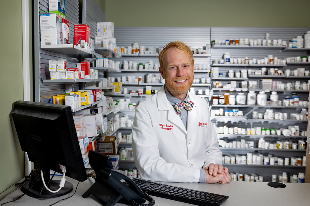 Ryan Bender in his white coat in front of shelves of medication