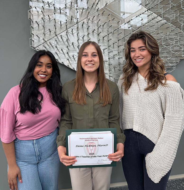Three individuals, with the one in the center holding a Teacher of the Year certificate