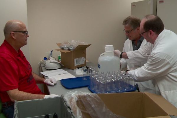 Paul Hutson, Barry Gidal, and Ed Elder gathered around a table filled with supplies to fill hand sanitizer bottles