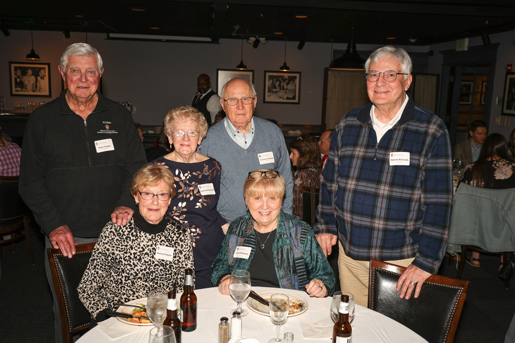 A group of older alumni sitting and standing at a table