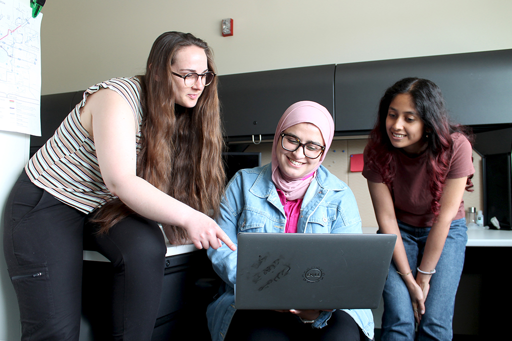Three students looking at a laptop together in an office