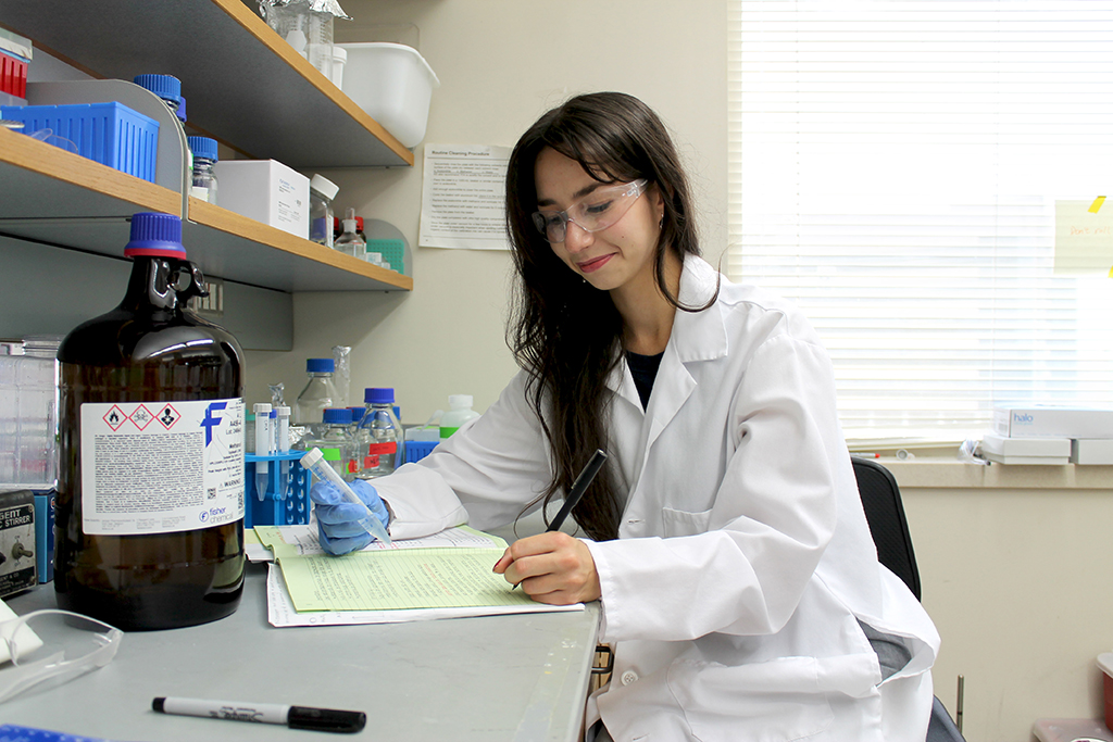 Sophia Melnyk wears a white coat and works with a test tube in a lab