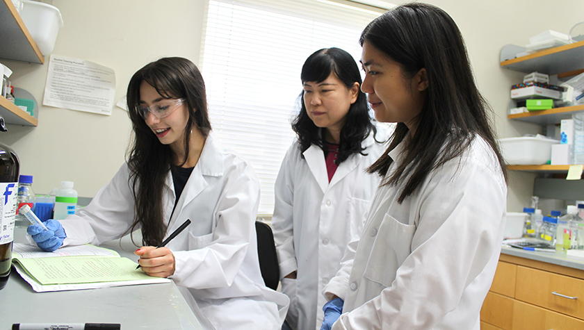 Three women in white coats work together in a lab