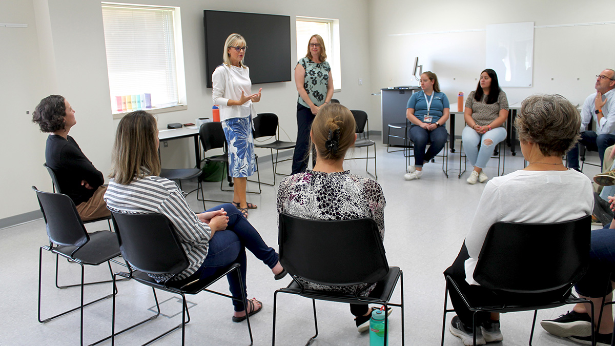 Beth Martin standing in the middle of a circle of seated faculty in chairs