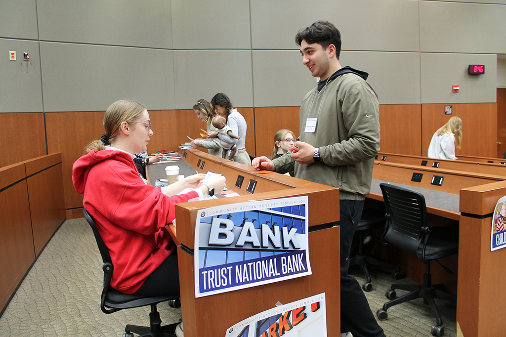 Students are stopping at a station labeled "Bank, Trust National Bank" during the poverty simulation.