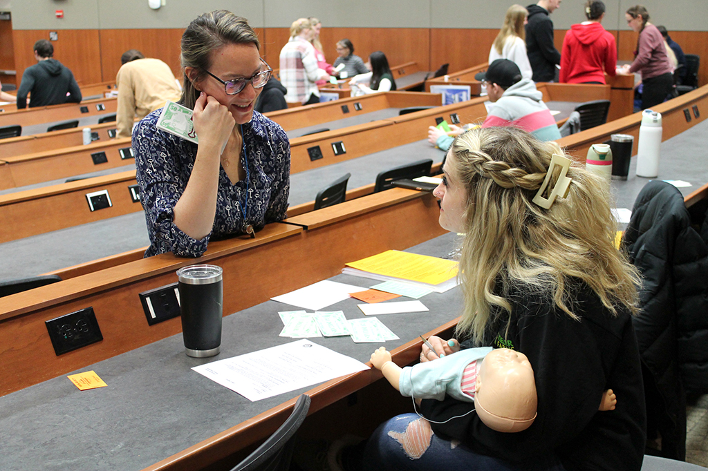 Associate Teaching Professor Kate Rotzenberg (PharmD '07) works with a PharmD student holding a baby doll during the poverty simulation. 
