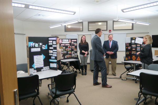 Provost Karl Scholz standing in the middle of a room with different informational boards about student organizations with student leaders nearby