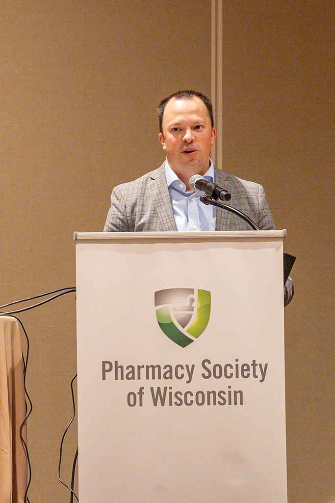 Jason Bergsbaken speaks at a podium with the Pharmacy Society of Wisconsin logo on it. 