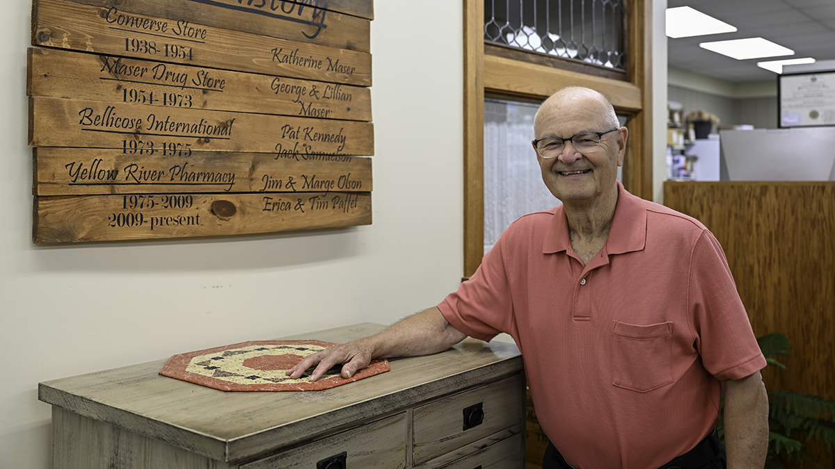 Jim Olson portrait next to a sign listing the previous names of the pharmacy