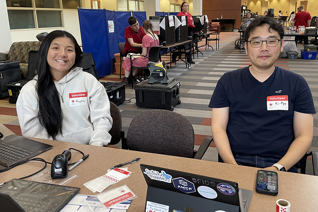 Virginia Quach and Ki-Pyo Hong smile while seated at a table in front of blood donation chairs in the background.