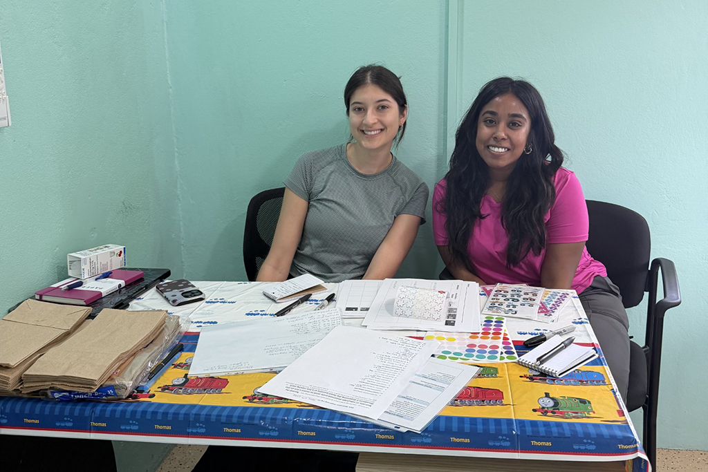 Jasmine Kuhnhenn and Sadiyya Rahaman sit at a table covered in papers and circular stickers