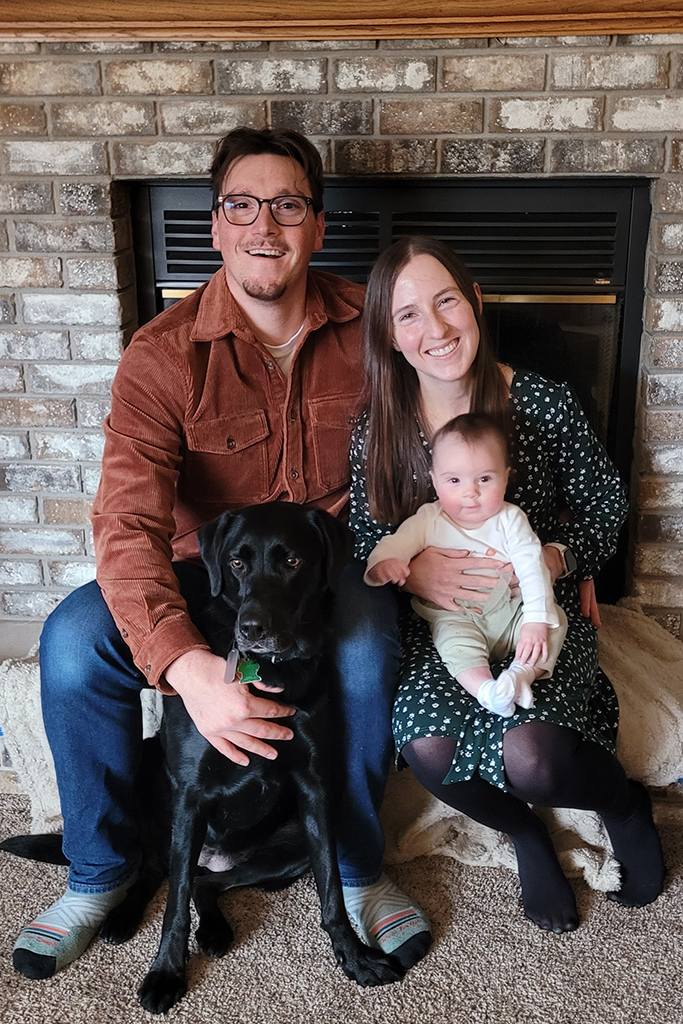 Katie Kuecker, husband, and infant pose in front of a fireplace
