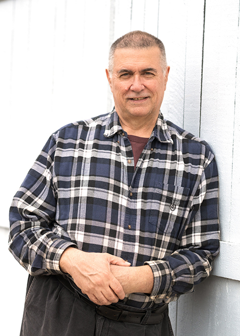 Mark Putzi leans against a wooden fence