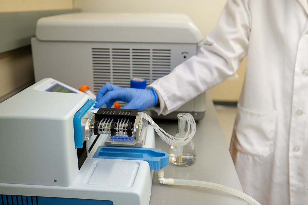 A blue-gloved hand adjusts a white machine with a black tray sticking into the front of it