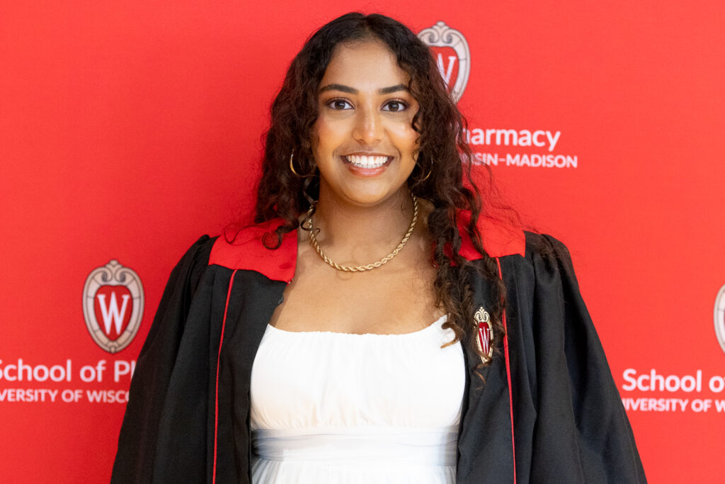 A PharmTox student poses with the red School of Pharmacy background.