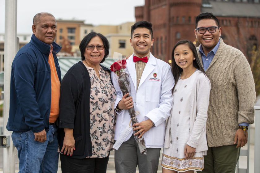 Student in white coat holding flowers with family after white coat ceremony