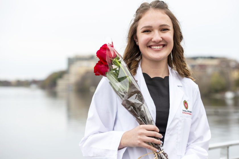Student in white coat smiling on the terrace with flowers after white coat ceremony