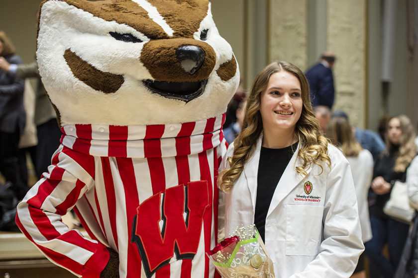 Student in white coat standing with Bucky Badger