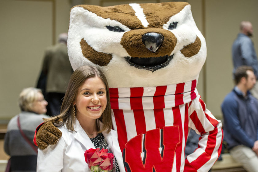 Student in white coat posing with Bucky after white coat ceremony