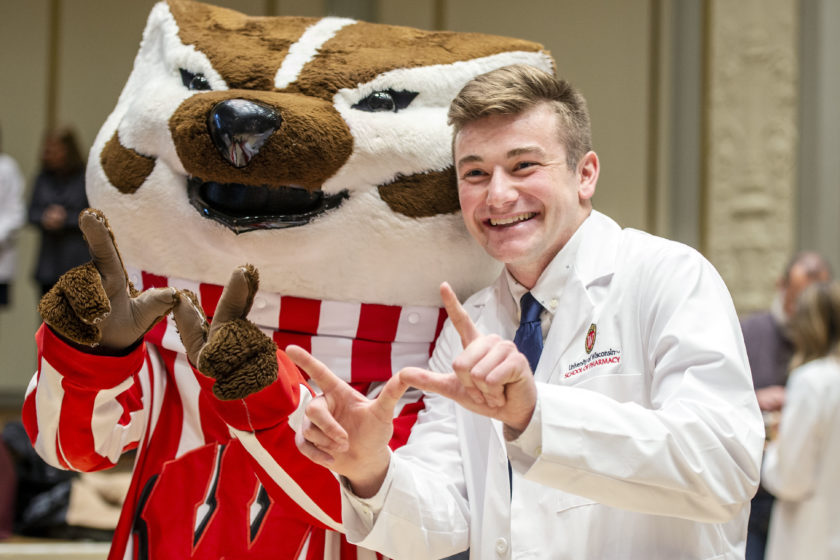 Student in white coat posing with Bucky after White Coat Ceremony