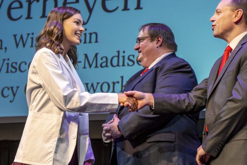 Student wearing white coat and shaking hands with staff during white coat ceremony