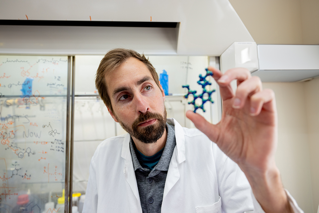 Cody Wenthur in a white coat, holding up a plastic molecule model