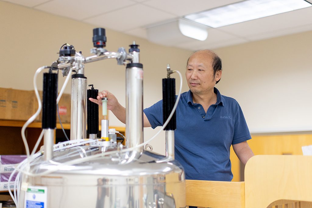 Sheng Cai adjusting tubing on top of a large silver tank with cylinders coming out of the top