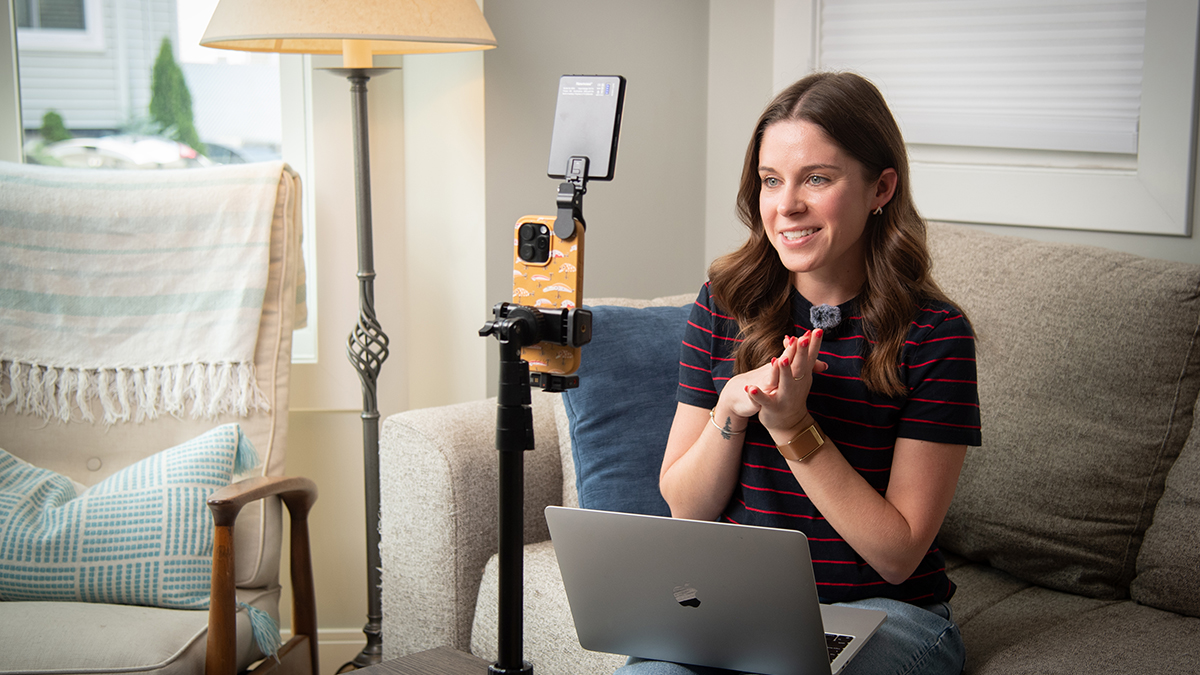 Rachel Hawley sits on her couch and speaks toward her phone, mounted on a tripod.