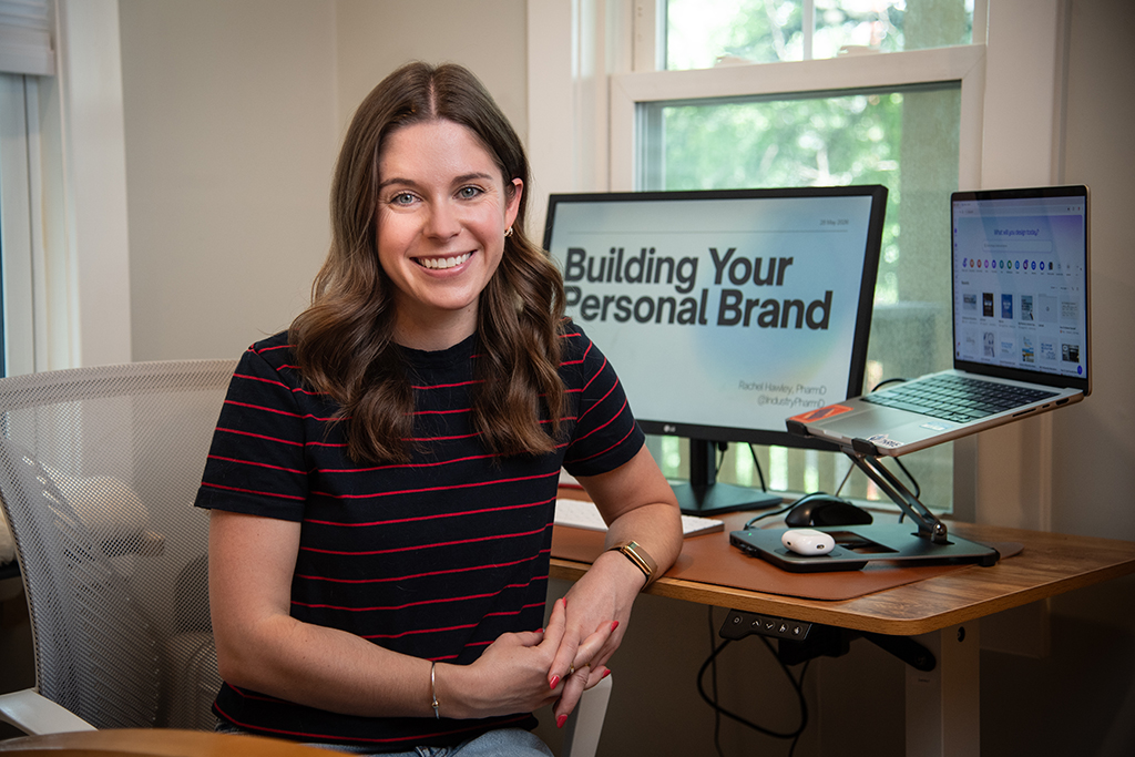 Rachel Hawley poses at her computer with two monitors, one of which reads "Building Your Personal Brand"