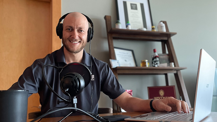 Ryan Feldman smiling at his desk with microphone and laptop in front of him