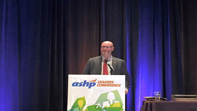 Steve Rough speaking at podium, M.S., FASHP, Senior Director of Pharmacy, UW Health, and Clinical Associate Professor, UW-Madison School of Pharmacy, presenting the 32nd John W. Webb Lecture at the Annual ASHP Conference for Pharmacy Leaders in October 2016 in Boston, Mass.