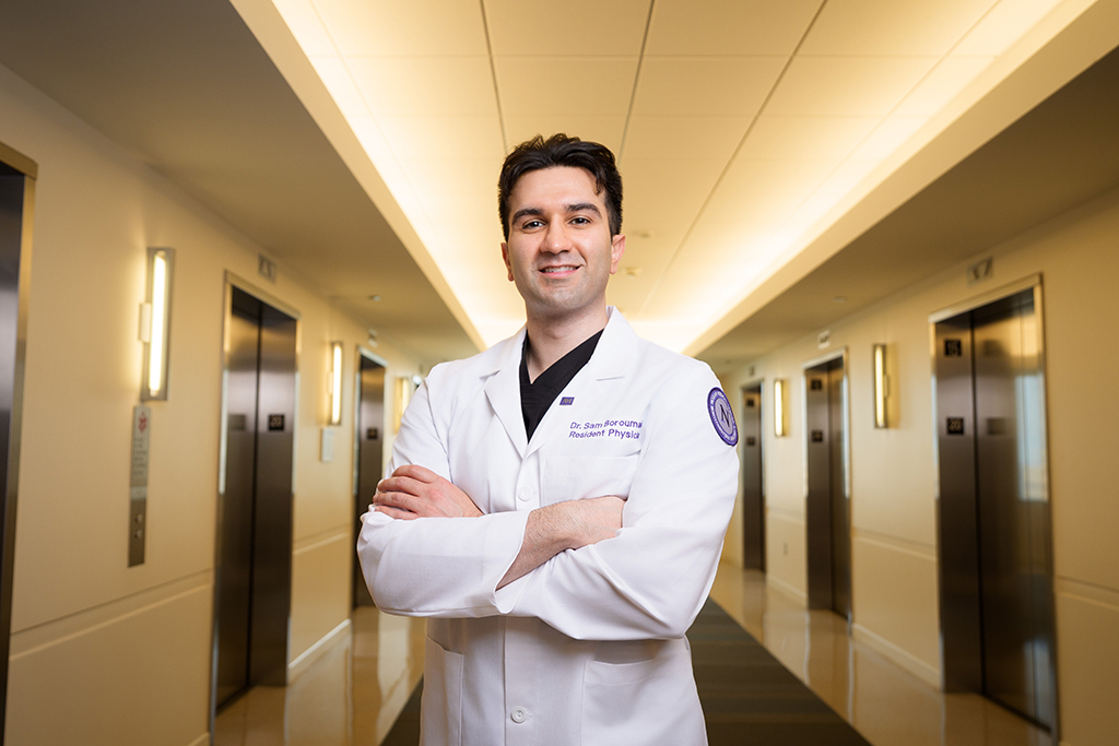 Sam Boroumand posing in a white coat in a hospital corridor