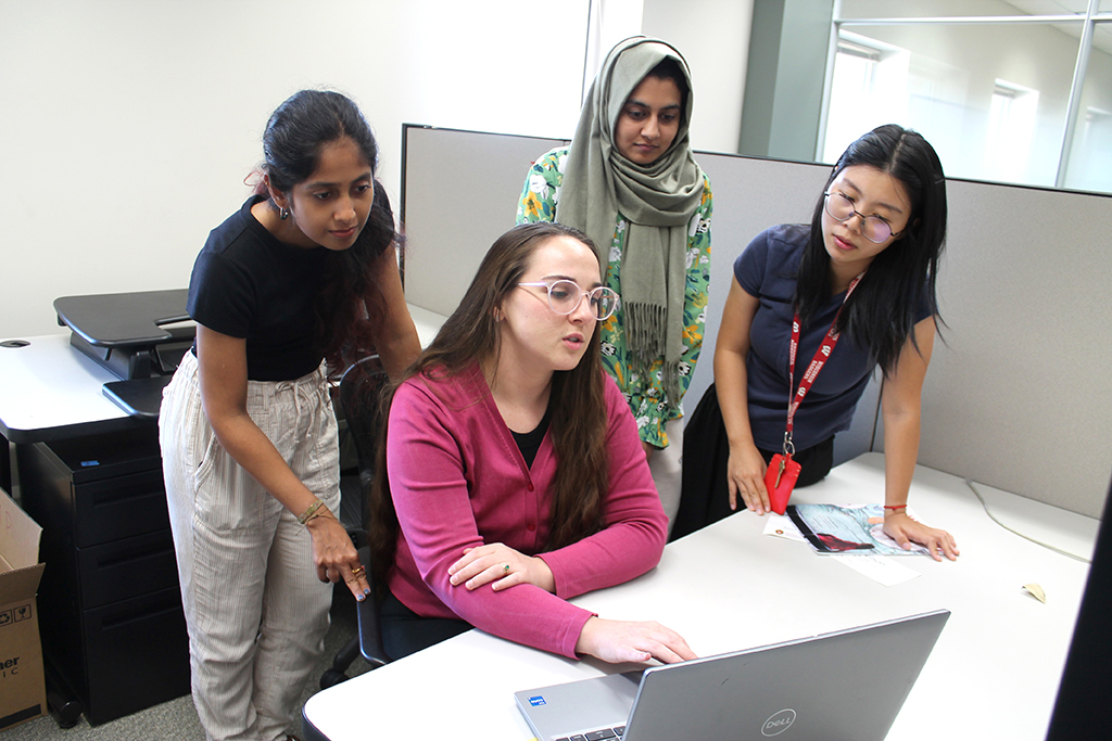 Sara Hernandez sits and works at a laptop surrounded by three other graduate students