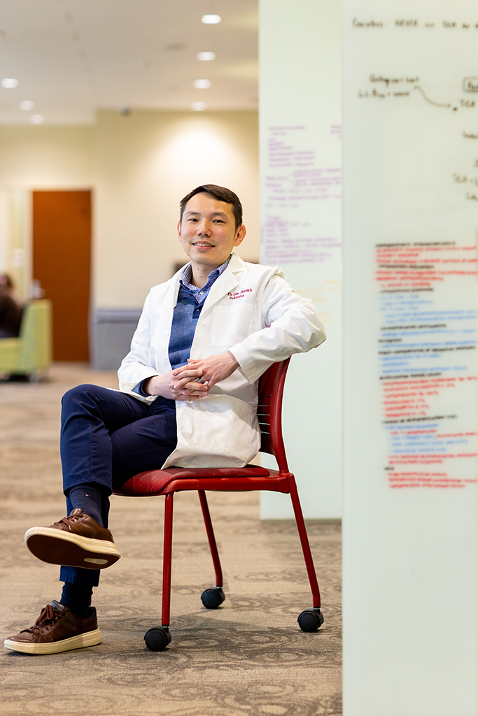 Sin Yin Lim sits in a chair in his white coat next to a white board of colorful notes