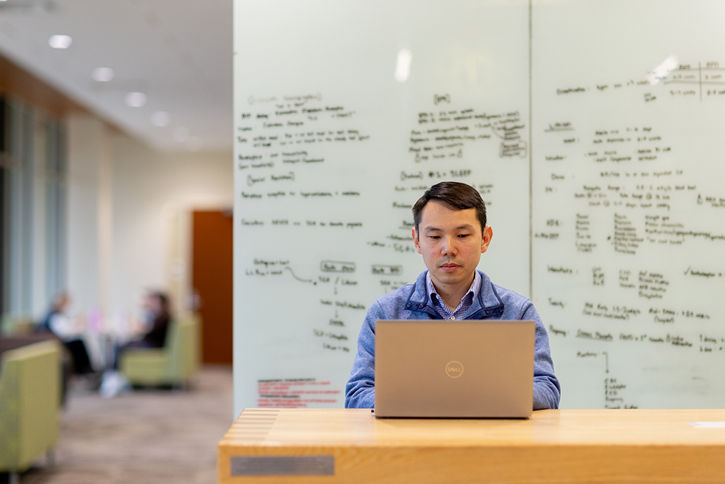 Sin Yin Lim works at his computer in front of a whiteboard filled with notes