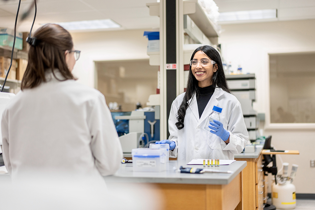 Apoorva Reddy wearing a white coat in goggles, working in a lab