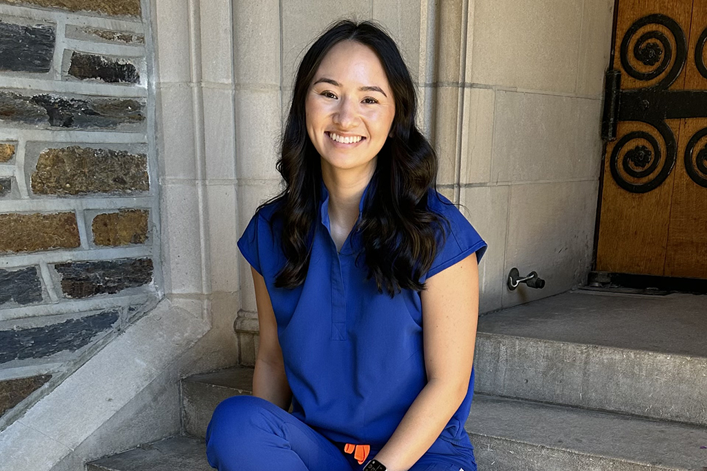 Shelby Koen in blue scrubs sitting on stairs