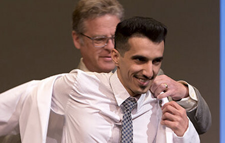 A professor helps a student into a coat at the White Coat Ceremony