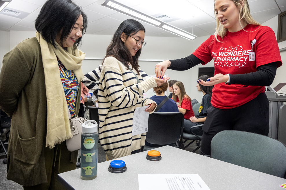 PharmD student Caitlin Cook hands some tokens to Diwasari Adani as she plays the PlinkRx game during the Wonders of Pharmacy on Saturday, March 2, 2024, at the School of Pharmacy on the campus of UW-Madison. (Photo Paul L. Newby, II)