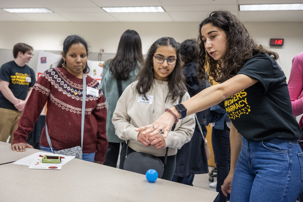 First-year PharmD student Nourhan El-Sanjak, right, explains where to roll the ball for a high score to Kavya Kashyap as her mother, Lalitha Kashyap, looks on as she plays the Pharmacy Pipeline activity during the Wonders of Pharmacy.