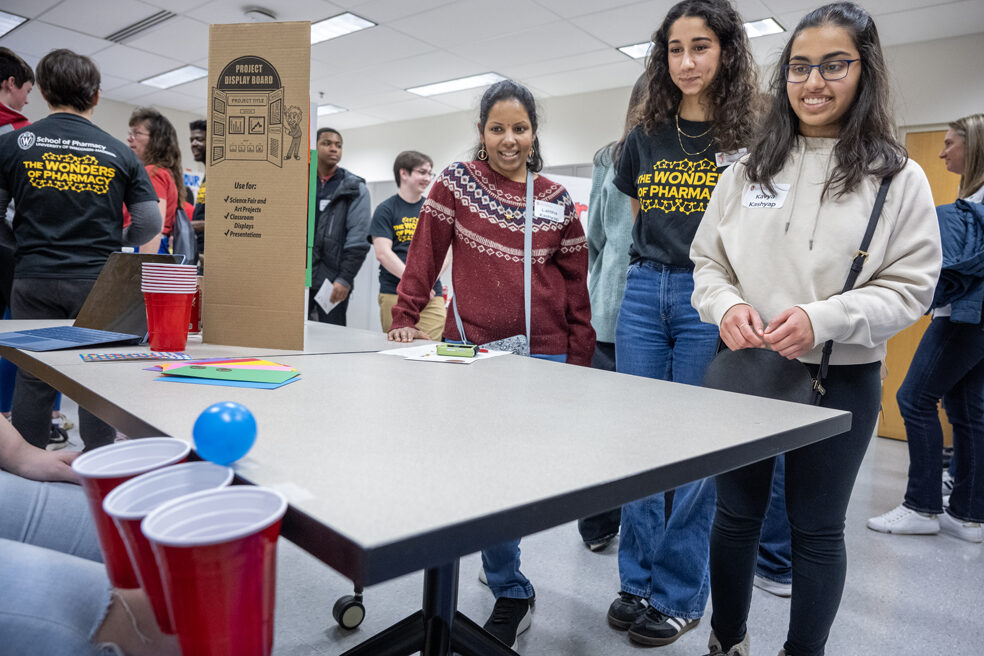 Kavya Kashyap watches her ball roll toward the cups as her mother, Lalitha Kashyap, and first-year PharmD student Nourhan El-Sanjak look on as she plays the Pharmacy Pipeline activity during the Wonders of Pharmacy on Saturday, March 2, 2024, at the School of Pharmacy on the campus of UW-Madison. (Photo Paul L. Newby, II)