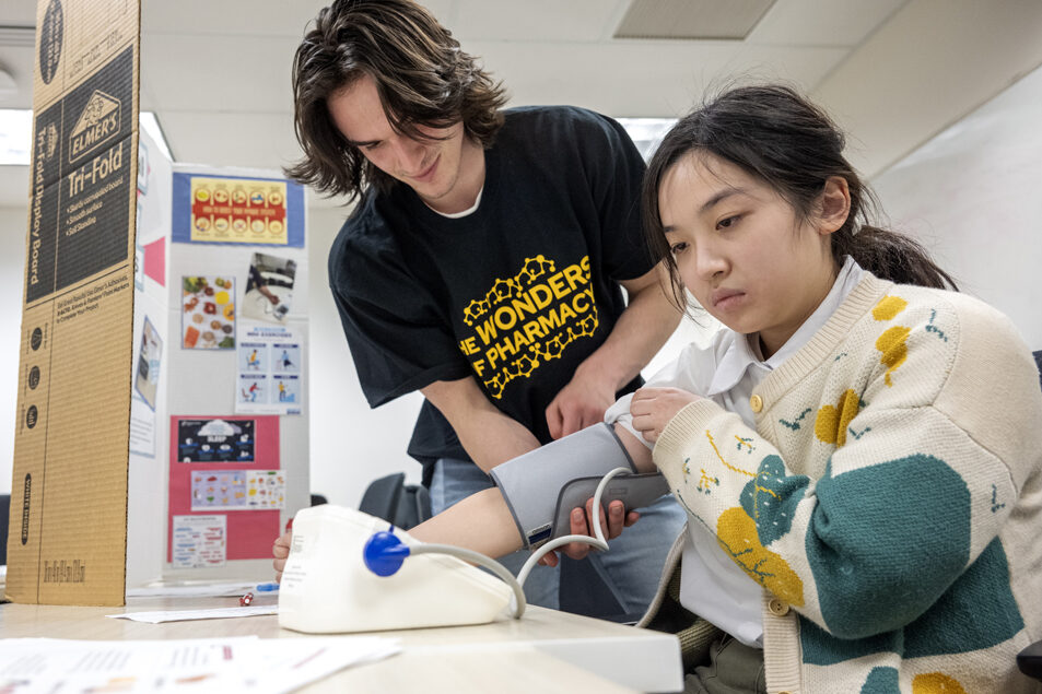 Third-year PharmD student Michael Milani helps Lisa Wang with the blood pressure cuff as she measures her blood pressure at the Operational PHP (Personal Health Partners) station during the Wonders of Pharmacy on Saturday, March 2, 2024, at the School of Pharmacy on the campus of UW-Madison. (Photo Paul L. Newby, II)