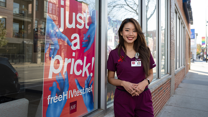 ThuyVu Do stands near a "just a prick" sign to encourage HIV testing.
