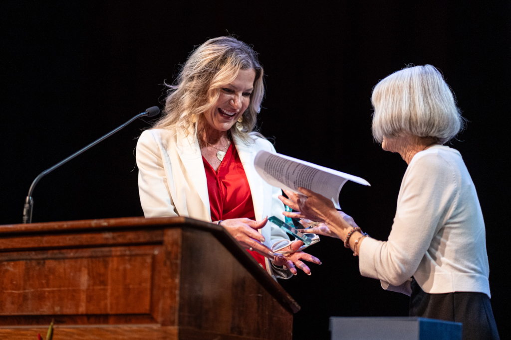 Trisha Ludwig smiles and receives an award from Mara Kieser behind a podium
