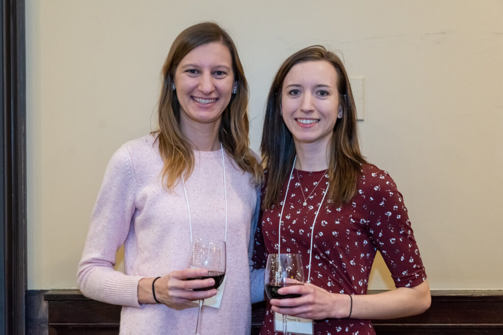 Two female alumni arm in arm with wine glasses